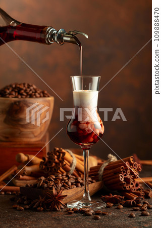 Coffee liquor is poured from a bottle into a glass with cream. 109888470