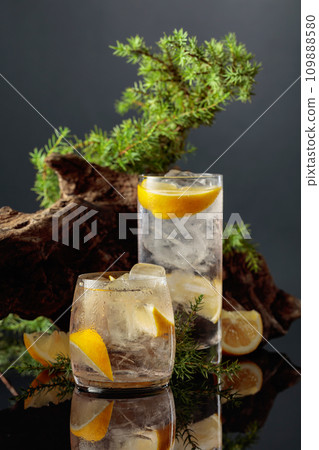 Cocktail gin-tonic with ice and lemon on a black reflective background. Cocktail gin-tonic with ice and lemon on a black reflective background. 109888580