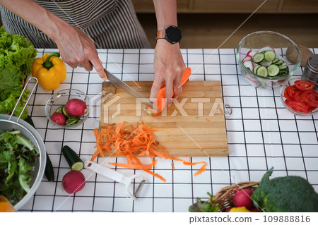 Above view of senior man cutting carrot on wooden board while preparing a healthy salad 109888816