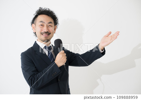 A businessman speaking with a microphone, looking at the camera in the image of a moderator A businessman speaking with a microphone, looking at the camera in the image of a moderator 109888959