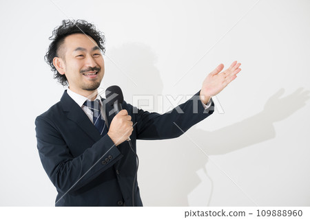 A businessman speaking with a microphone, looking at the camera in the image of a moderator A businessman speaking with a microphone, looking at the camera in the image of a moderator 109888960