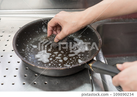 A man scrubs a Teflon-coated frying pan with a metal scrubber 109890234