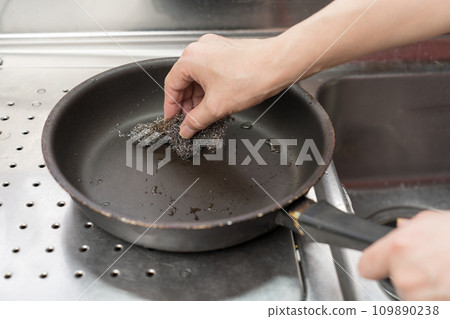 A man scrubs a Teflon-coated frying pan with a metal scrubber 109890238