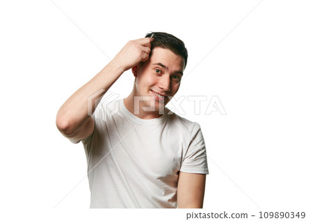 Portrait of attractive young man looks at camera and smile while combing his hair against white background. Concept of hair care and barber. Portrait of attractive young man looks at camera and smile while combing his hair against white background. Concept of hair care and barber. 109890349
