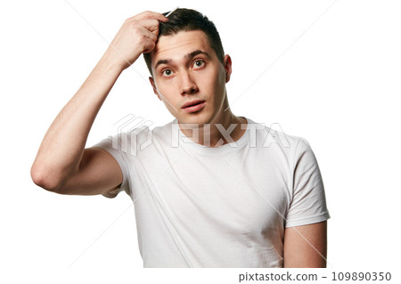 Portrait of attractive young man looks at camera in surprise while combing his hair against white background. Concept of hair care, barber. 109890350