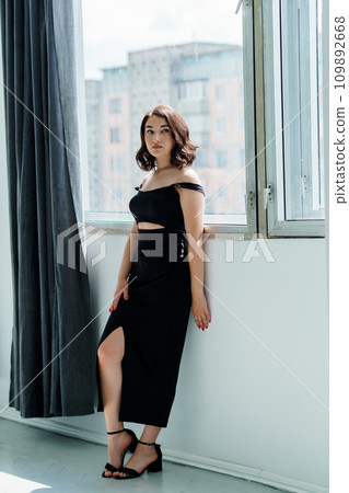 Portrait of a young girl in a black dress standing by the window Portrait of a young girl in a black dress standing by the window 109892668