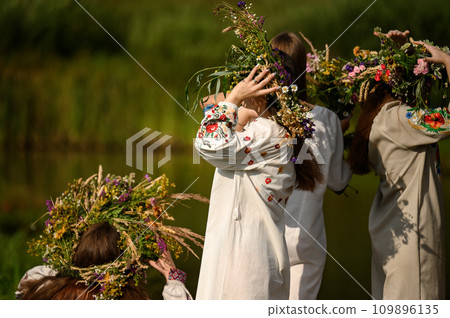 Girls in woven wreaths of different flowers and grass on a warm summer day. Girls in woven wreaths of different flowers and grass on a warm summer day. 109896135