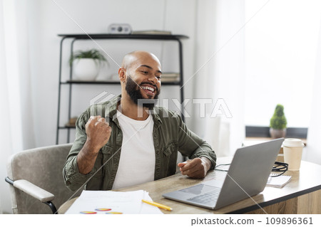 Great job. Happy latin man looking at laptop and expressing emotions of victory, sitting at desk at home office Great job. Happy latin man looking at laptop and expressing emotions of victory, sitting at desk at home office 109896361