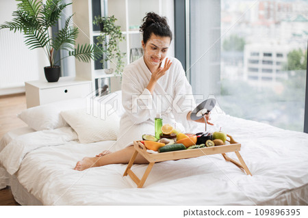 Relaxed adult person in after-shower wear applying facial mask Relaxed adult person in after-shower wear applying facial mask 109896395