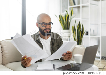 Latin male entrepreneur working from home, getting ready for presentation, sitting in front of laptop with papers 109896449