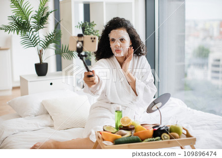 Young female influencer in paper sheet mask holding smartphone 109896474