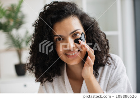 African-american woman in white bathrobe fixing black gel patch with finger 109896526