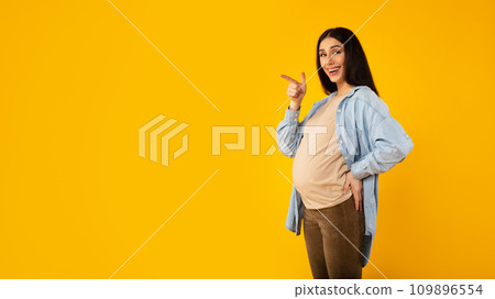 Cool offer. Happy pregnant woman pointing aside at free space, standing over yellow background, panorama Cool offer. Happy pregnant woman pointing aside at free space, standing over yellow background, panorama 109896554