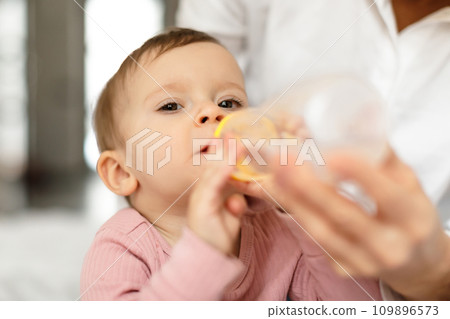 Caring mother giving water bottle to her little baby girl, closeup shot 109896573