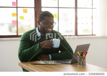 African Male Designer Working On Laptop Drinking Coffee In Office 109896600