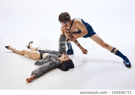 Young woman lies on floor in weird, revealing costume and pushes away guy hanging over her in same strange outfit Young woman lies on floor in weird, revealing costume and pushes away guy hanging over her in same strange outfit 109896731
