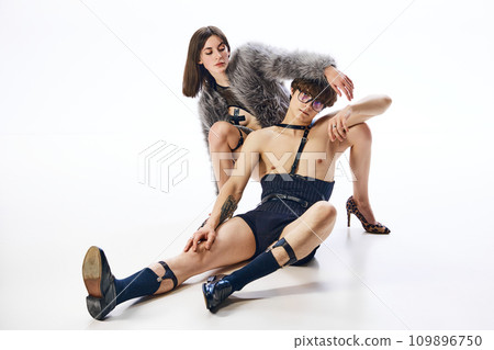 Portrait of confident couple, man and woman in love, posing sitting in freaky provocative outfits against white background. Portrait of confident couple, man and woman in love, posing sitting in freaky provocative outfits against white background. 109896750