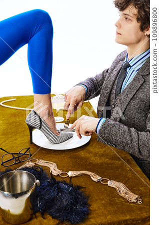 Aristocratic man, young guy in office suit eating female leg in blue leggings like delicious dish in restaurant. Aristocratic man, young guy in office suit eating female leg in blue leggings like delicious dish in restaurant. 109896800