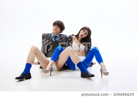 Attractive young people dressed in stylish, bright and fancy outfits sitting on floor and posing against white studio background. 109896829