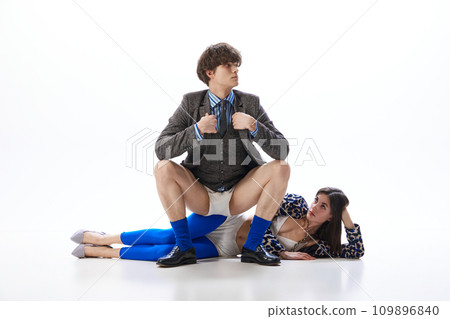Young man in suit but without trousers but in underwear sits on hip of girl in blue glamorous tights and animal printed jacket. 109896840