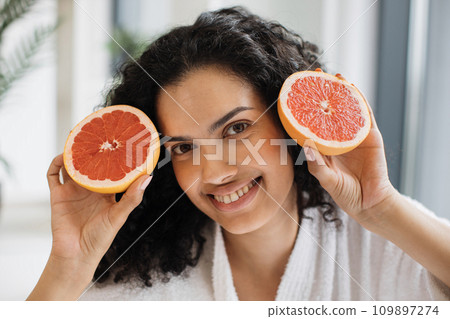 Healthy female holding two halves of grapefruit near cheeks 109897274