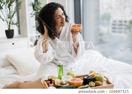 Lady looking at citrus half while sitting in bedroom 109897325