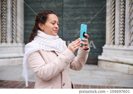 Happy woman photographing the medieval Italian city of Como, standing against the door of Santa Maria Maggiore cathedral 109897601