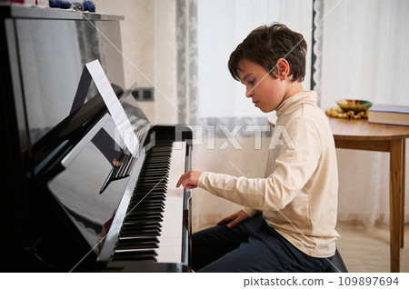 Caucasian handsome teenage boy playing piano at home, sitting and performing classical musical composition 109897694