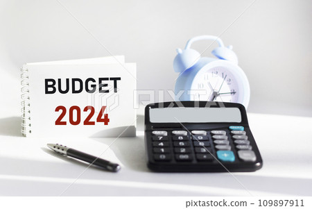 BUDGET 2024 written on a notepad and white background and with a calculator clock 109897911