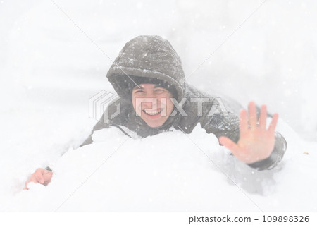 a boy lies in the snow, on a snowy street, it is snowing, a blizzard and frost on a winter day 109898326