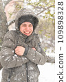a boy is posing with snow on the street, it is snowing, a blizzard and frost on a winter day 109898328
