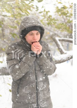 a boy is posing with snow on the street, it is snowing, a blizzard and frost on a winter day, he warms his hands with his breath a boy is posing with snow on the street, it is snowing, a blizzard and frost on a winter day, he warms his hands with his breath 109898330