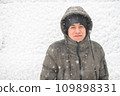 a boy is posing on snow background outdoor, it is snowing, a blizzard and frost on a winter day 109898331