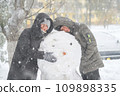 a girl and a boy is playing with snow on the street, making snowman, it is snowing, a blizzard and frost on a winter day 109898335