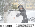 a girl is playing with snow on the street, making snowman, it is snowing, a blizzard and frost on a winter day 109898337