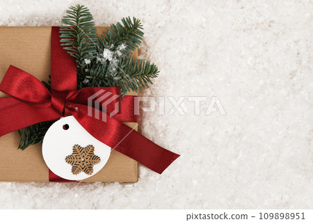 Card with gift box with fir tree sprig and label with snowflake on snow background. Space for your text. Card with gift box with fir tree sprig and label with snowflake on snow background. Space for your text. 109898951