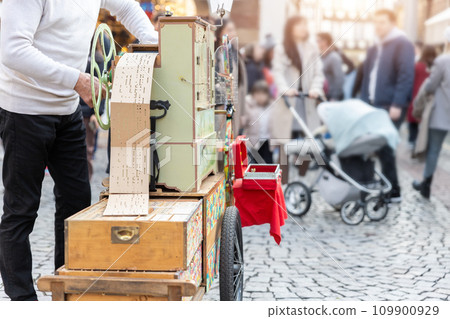 Street artist busker man playing music by organ barrel vintage wooden box machine at crowded old european city France. Person musician grinder busking with retro music instrument tool outdoors Street artist busker man playing music by organ barrel vintage wooden box machine at crowded old european city France. Person musician grinder busking with retro music instrument tool outdoors 109900929