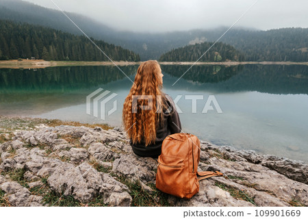 Woman Sitting Alone on Rock by Mountain Lake 109901669
