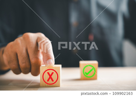 Businessman finger touches wooden cubes with wrong cross X for right. Shows communication of choice validation in decision-making. Think With Yes Or No Choice. 109902163