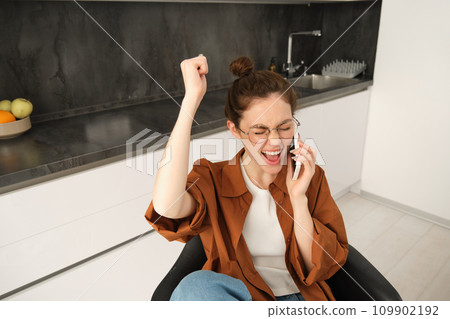 Happy woman receive positive news, job offer over phone call, celebrating, sitting at home, talking on telephone with rejoice, dancing on her seat Happy woman receive positive news, job offer over phone call, celebrating, sitting at home, talking on telephone with rejoice, dancing on her seat 109902192