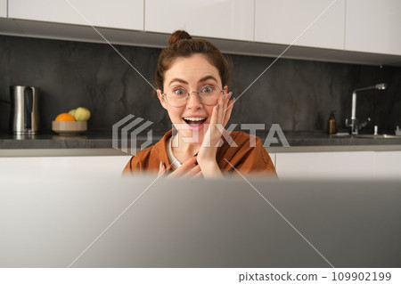 Close up portrait of amazed young woman, looking at laptop with happy, surprised face expression, sitting at home 109902199