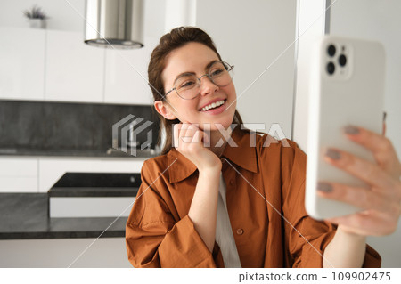 Happy smiling woman in glasses, taking selfie, recording video on smartphone, video chats on mobile phone application Happy smiling woman in glasses, taking selfie, recording video on smartphone, video chats on mobile phone application 109902475