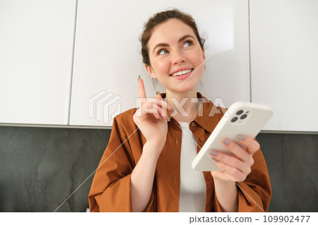 Portrait of beautiful young woman, smiling with pleased face, thinking, using smartphone application 109902477