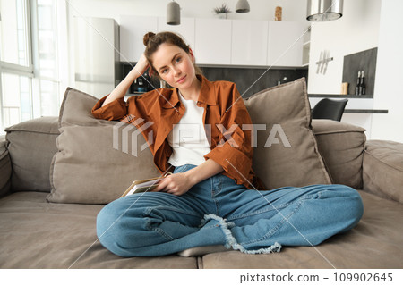 Portrait of young modern woman, female student sitting at home on sofa and looking at camera, posing on couch, smiling Portrait of young modern woman, female student sitting at home on sofa and looking at camera, posing on couch, smiling 109902645