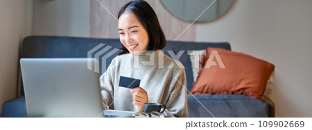 Portrait of korean woman shopping online, using her credit card and laptop to order delivery from website 109902669