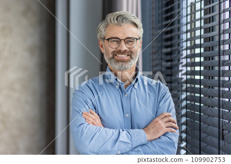 Portrait of mature successful businessman boss, senior gray-haired man inside office smiling looking at camera with crossed arms, experienced financier banker accountant in shirt. Portrait of mature successful businessman boss, senior gray-haired man inside office smiling looking at camera with crossed arms, experienced financier banker accountant in shirt. 109902753