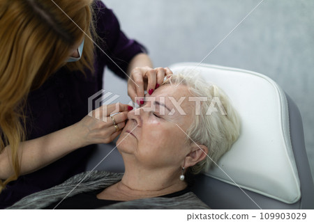 An apprentice at a beauty salon practices eyelash coloring on a model. 109903029