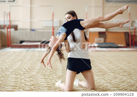 Coach with student. Girls gymnasts, performs various gymnastic exercises and jumping. Childs and sport, a healthy lifestyle. Coach with student. Girls gymnasts, performs various gymnastic exercises and jumping. Childs and sport, a healthy lifestyle. 109904128