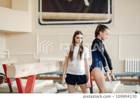 Child gymnastics balance beam. Girl gymnast athlete during an exercise horizontal bar in gymnastics competitions. Coach with child. Child gymnastics balance beam. Girl gymnast athlete during an exercise horizontal bar in gymnastics competitions. Coach with child. 109904130