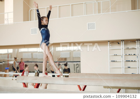 Child gymnastics balance beam. Girl gymnast athlete during an exercise horizontal bar in gymnastics competitions. Child gymnastics balance beam. Girl gymnast athlete during an exercise horizontal bar in gymnastics competitions. 109904132
